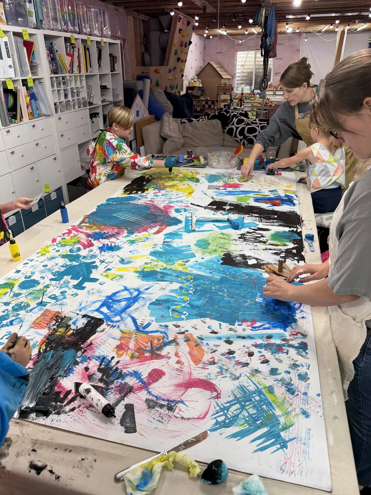 Students working across a large shared painting covered in colorful marks