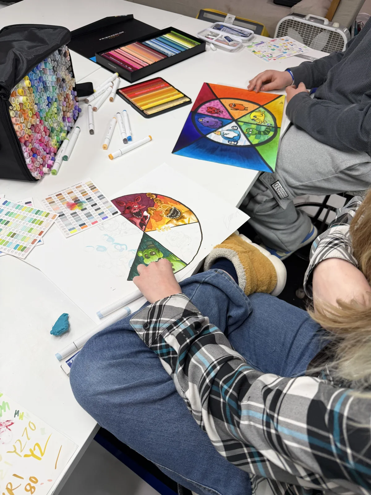 A teen artist developing a colorful character wheel, with their head and artwork visible