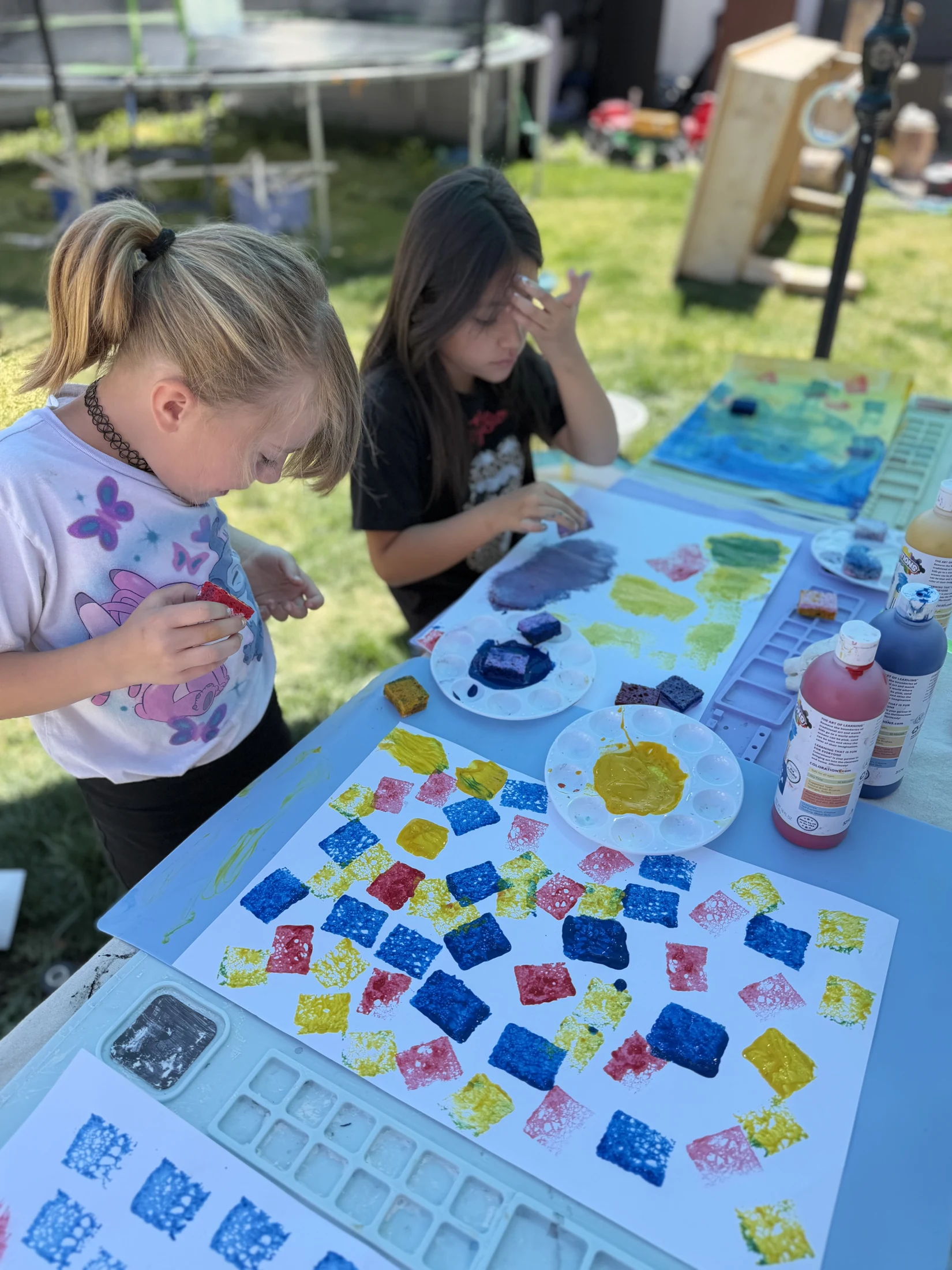 Two children exploring colorful printmaking outdoors