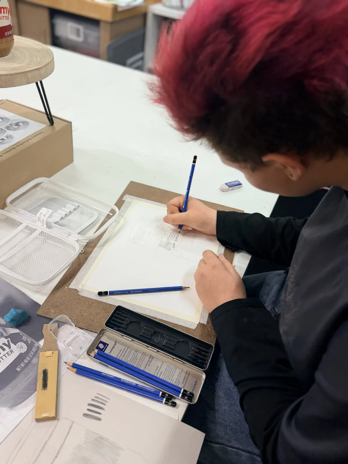 An older artist concentrating on a pencil study with drawing materials beside them
