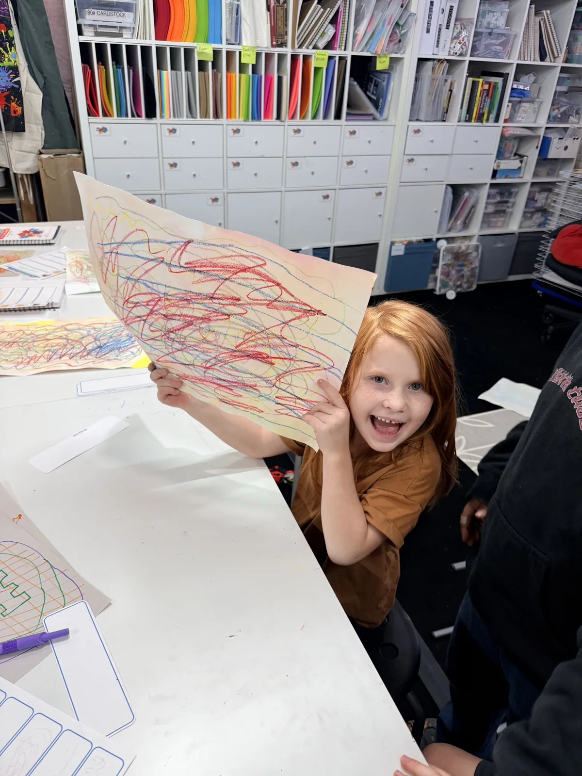 A smiling young artist holding up a colorful drawing in the Creative Roots studio