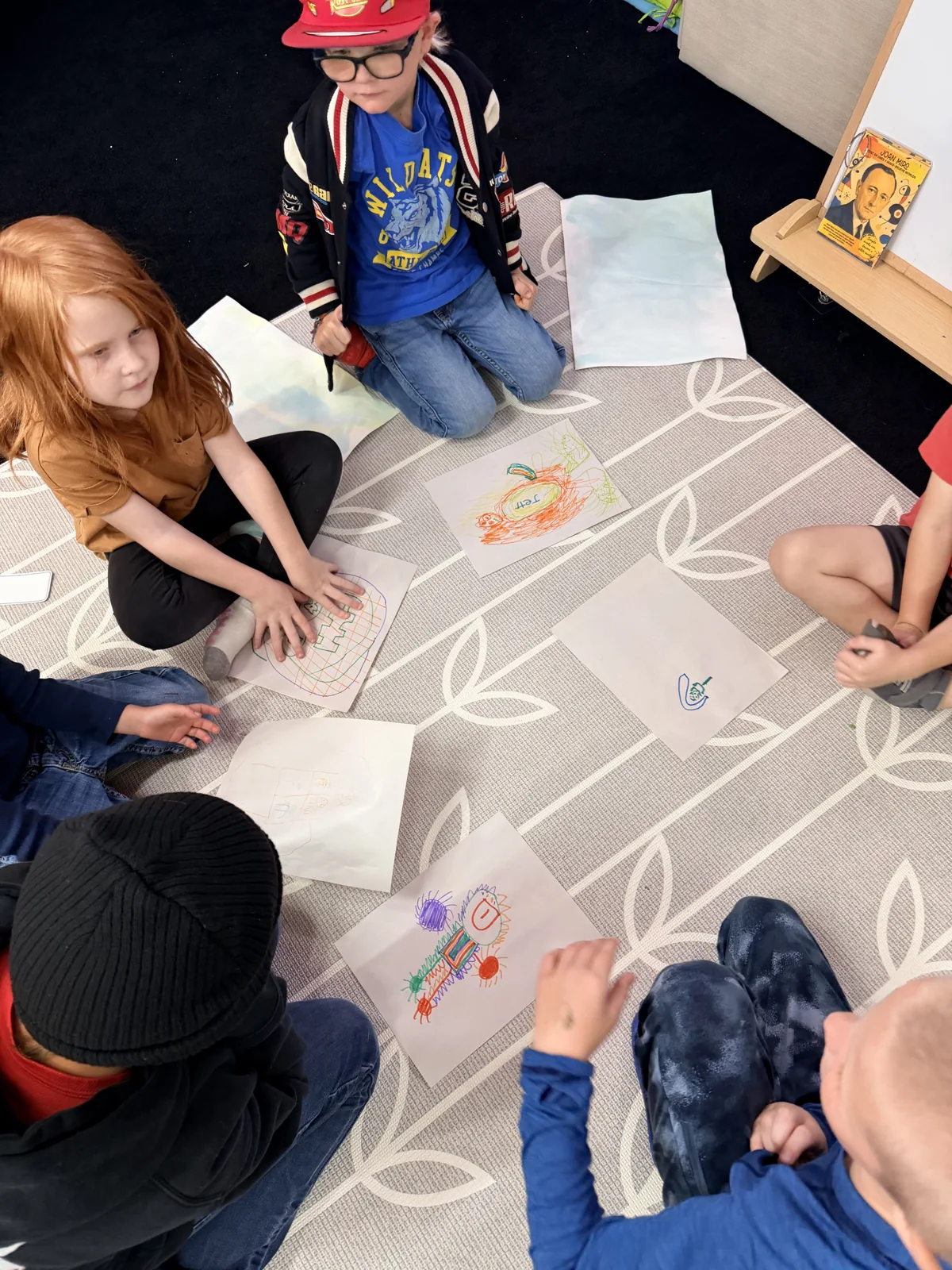 Young artists gathered around a large drawing on the studio floor